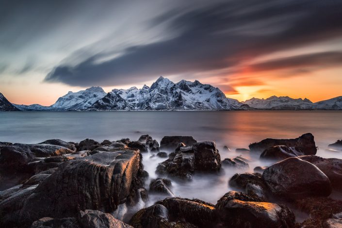 felsige Küste mit verschneiten Bergen bei Sonnenuntergang, Vareid, Lofoten